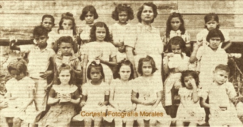 estudiantes de primer grado del barrio parís con la maestra antonia irizarry de díaz (primera fila) rita rivera, cuchi pabón, eddie blanco, luisa rodríguez, virgenmina rivera, nereida blanco, efraín sanoguet; (segunda fila) pito morales, divina flores, (tercera fila) obed morales, anita sanoguet, irma barros, gladys rivera, henrique y monserrate. (circa 1941-42). (cortesía de fotografía morales).